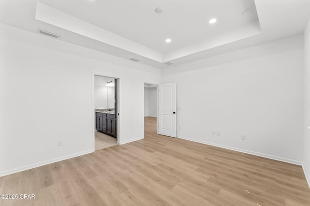 unfurnished bedroom with light wood finished floors, visible vents, a raised ceiling, and baseboards