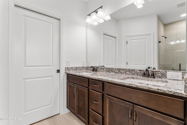 full bathroom with double vanity, tiled shower, visible vents, and a sink