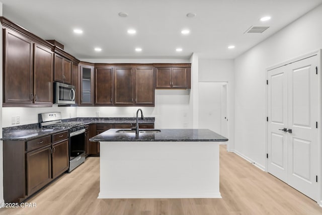 kitchen featuring visible vents, dark stone counters, light wood-style floors, stainless steel appliances, and a sink