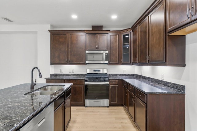 kitchen featuring visible vents, dark stone counters, light wood-style flooring, a sink, and stainless steel appliances