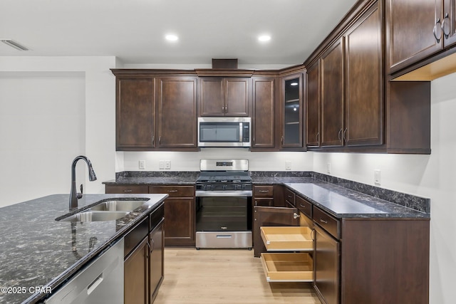 kitchen with dark stone countertops, visible vents, a sink, appliances with stainless steel finishes, and light wood-type flooring