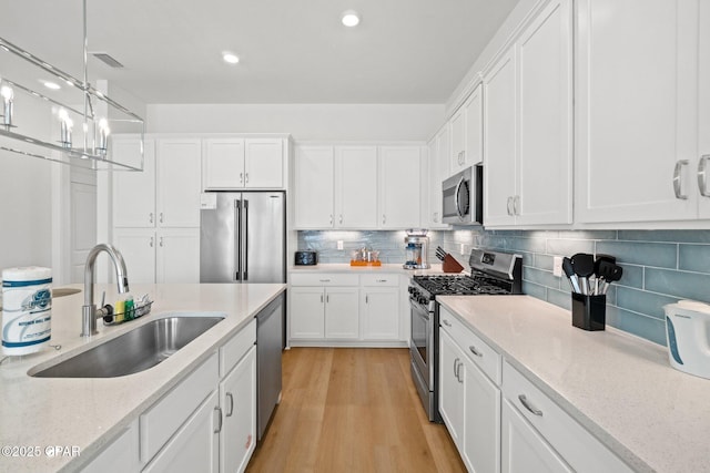 kitchen with a sink, white cabinets, light wood-type flooring, and stainless steel appliances