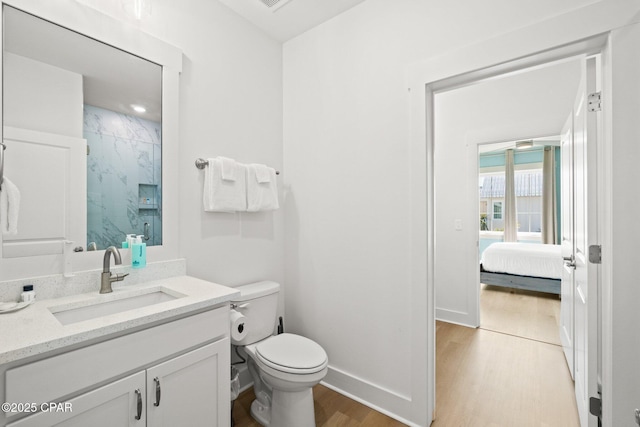 bathroom with vanity, wood finished floors, baseboards, a marble finish shower, and toilet