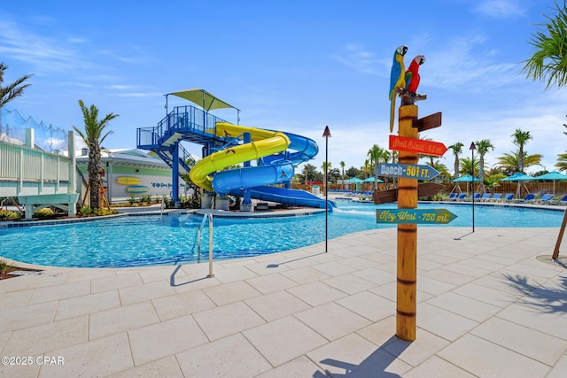 pool with a patio area, a water play area, a water slide, and fence