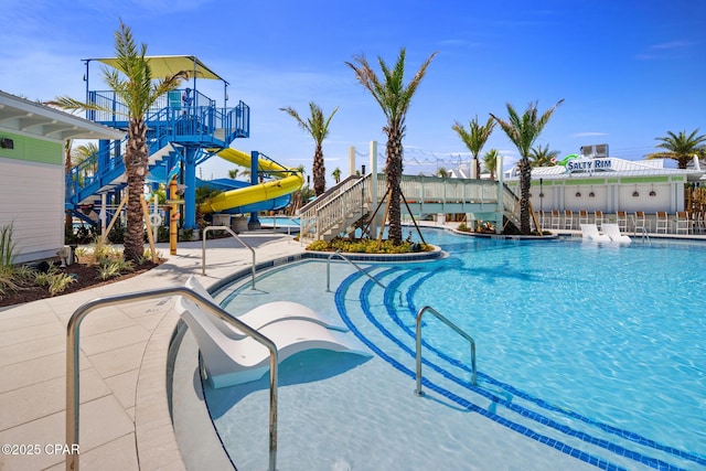 community pool with stairs, a patio area, and a water slide