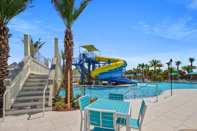 community pool featuring a water slide, stairs, and a patio area