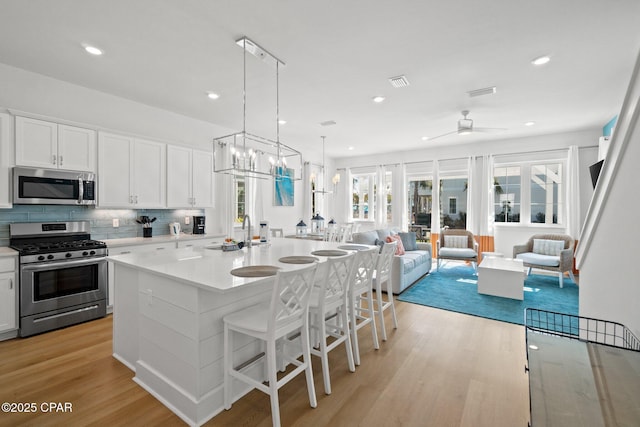 kitchen featuring stainless steel appliances, tasteful backsplash, open floor plan, and light wood-style flooring