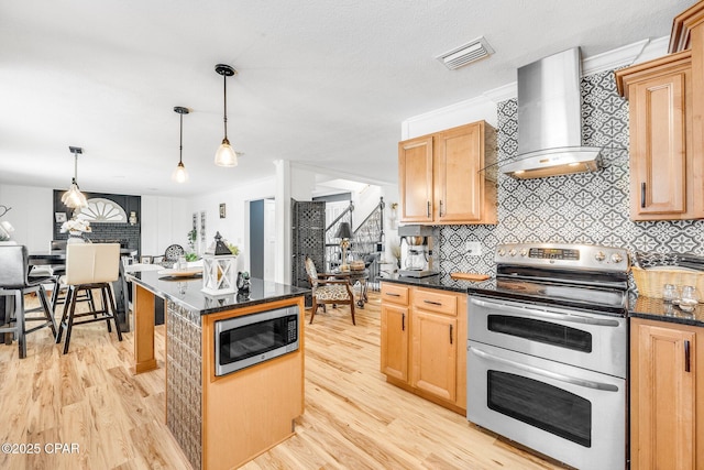 kitchen featuring light wood finished floors, visible vents, decorative backsplash, stainless steel appliances, and wall chimney exhaust hood