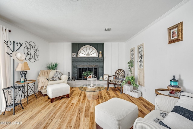 living area with visible vents, crown molding, a fireplace, wood finished floors, and a textured ceiling