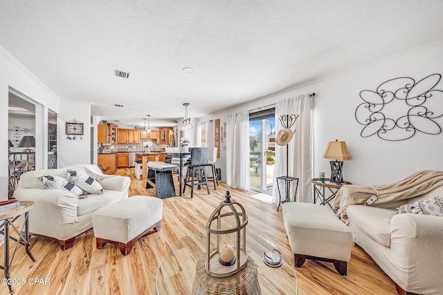 living room with visible vents, light wood-style flooring, and a textured ceiling