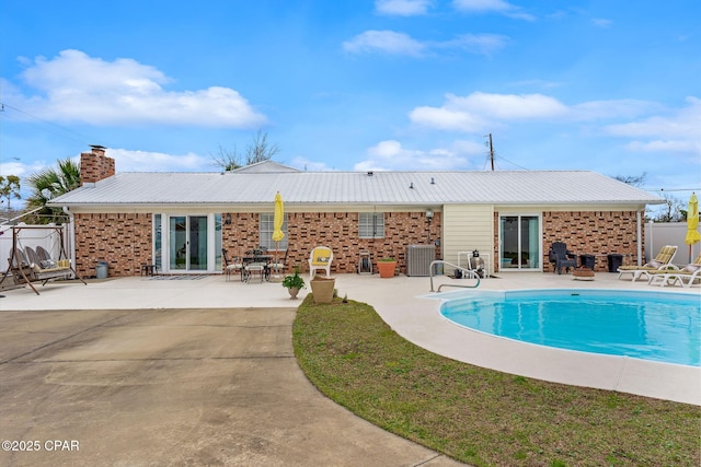 back of property with a patio, cooling unit, a fenced in pool, brick siding, and a chimney