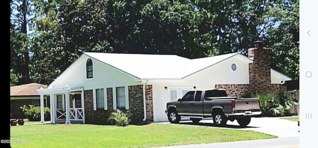 view of front facade with stone siding, driveway, a chimney, and a front yard