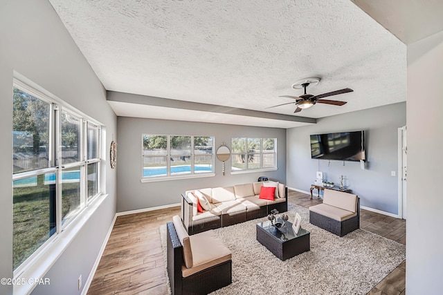 living room featuring a ceiling fan, wood finished floors, baseboards, and a textured ceiling