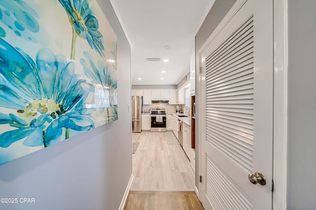 hallway with baseboards, visible vents, light wood finished floors, recessed lighting, and a sink