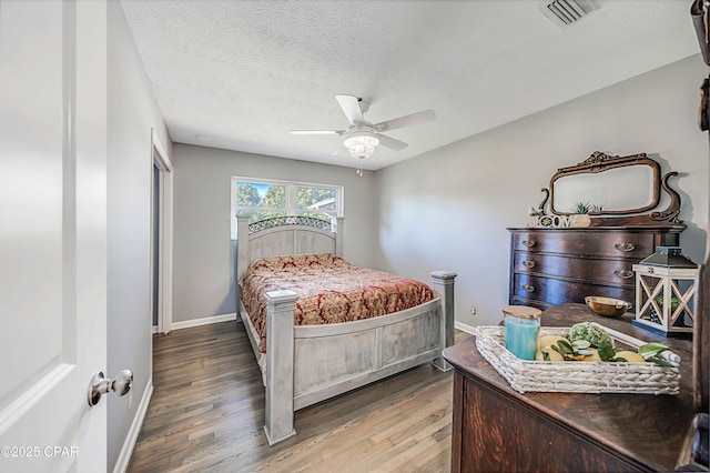 bedroom with visible vents, baseboards, wood finished floors, a textured ceiling, and a ceiling fan