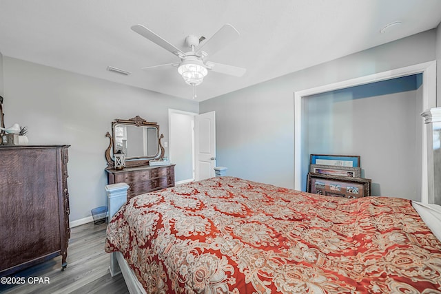 bedroom with ceiling fan, visible vents, baseboards, and wood finished floors