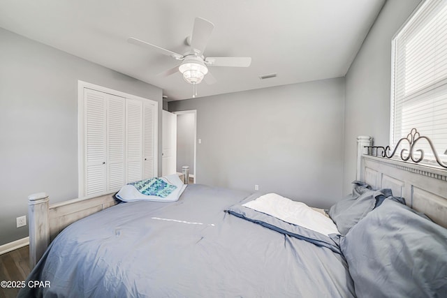 bedroom with visible vents, a ceiling fan, wood finished floors, a closet, and baseboards