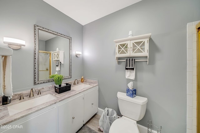 bathroom with double vanity, toilet, a shower with shower door, and a sink