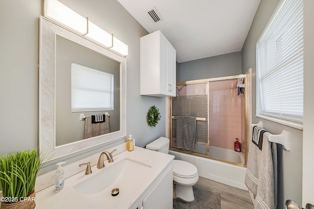 bathroom with visible vents, toilet, vanity, and shower / bath combination with glass door