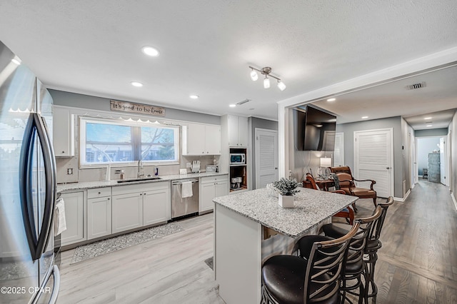 kitchen with visible vents, light wood-type flooring, a kitchen breakfast bar, stainless steel appliances, and a sink