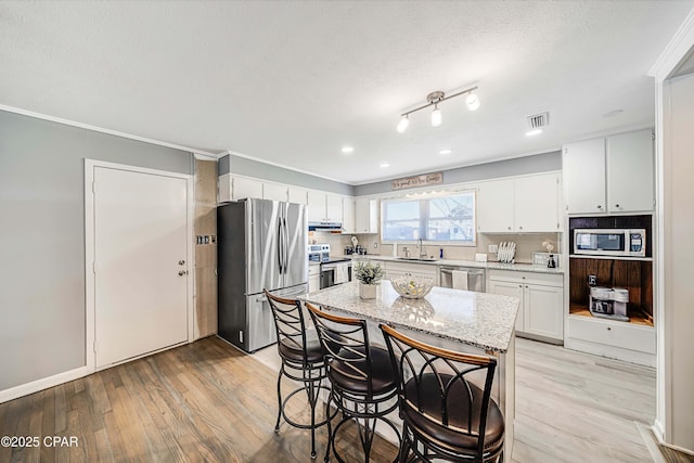 kitchen with visible vents, a sink, stainless steel appliances, light wood-style floors, and white cabinetry