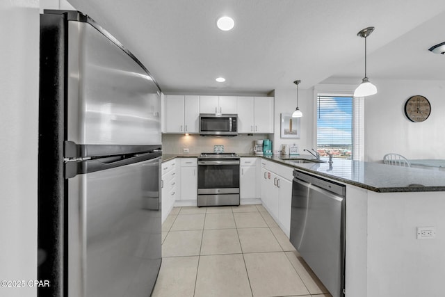 kitchen with dark stone counters, a peninsula, appliances with stainless steel finishes, light tile patterned flooring, and white cabinets