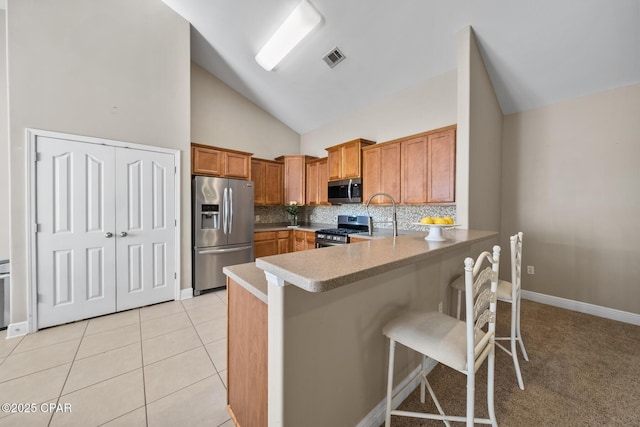 kitchen with light tile patterned floors, a peninsula, a sink, appliances with stainless steel finishes, and tasteful backsplash