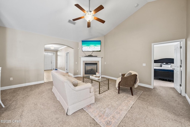 carpeted living area with visible vents, baseboards, ceiling fan, a fireplace, and arched walkways