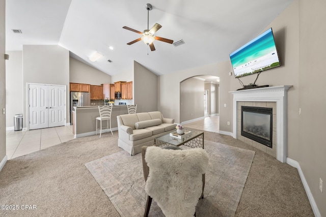 living area featuring light tile patterned floors, visible vents, arched walkways, ceiling fan, and light colored carpet