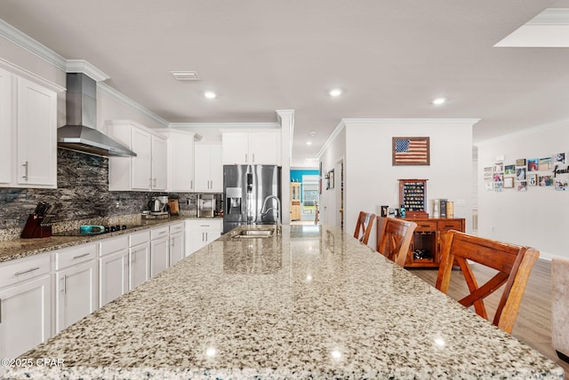 kitchen featuring visible vents, a sink, stainless steel fridge with ice dispenser, wall chimney range hood, and black electric cooktop