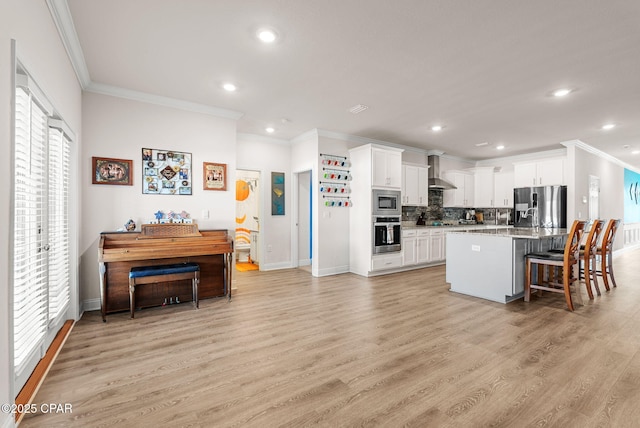 kitchen featuring light wood finished floors, backsplash, wall chimney range hood, stainless steel appliances, and white cabinetry