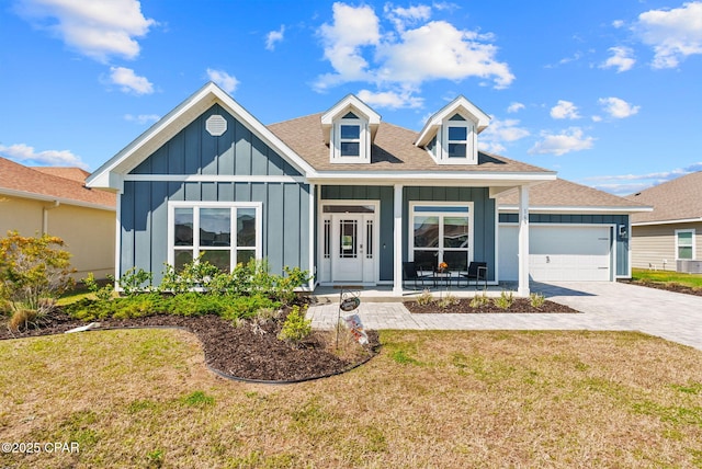 view of front of house featuring board and batten siding, a front lawn, a porch, decorative driveway, and a garage