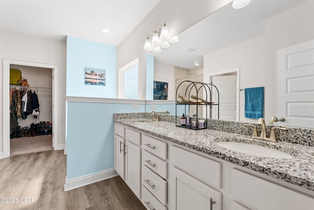 bathroom with double vanity, wood finished floors, a walk in closet, and a sink