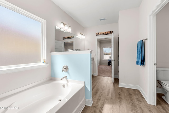 bathroom with a bath, wood finished floors, visible vents, baseboards, and toilet