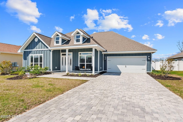 view of front of property featuring board and batten siding, a front yard, covered porch, decorative driveway, and an attached garage