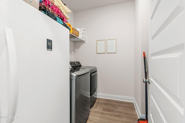 clothes washing area with washer and dryer, baseboards, wood finished floors, and laundry area