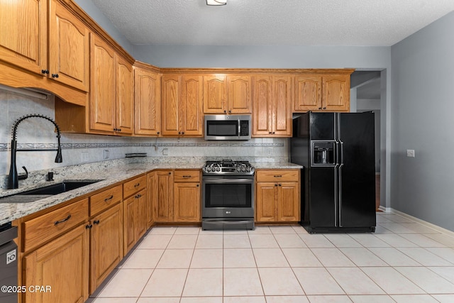 kitchen featuring tasteful backsplash, light stone counters, appliances with stainless steel finishes, brown cabinetry, and a sink