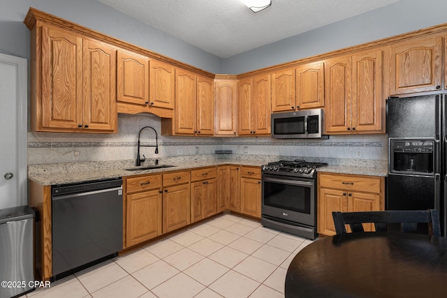 kitchen with black appliances, light stone counters, backsplash, and a sink