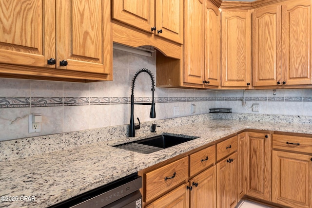 kitchen with tasteful backsplash, light stone countertops, dishwasher, and a sink