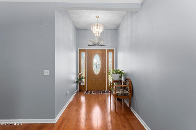 foyer entrance with hardwood / wood-style flooring, a notable chandelier, and baseboards