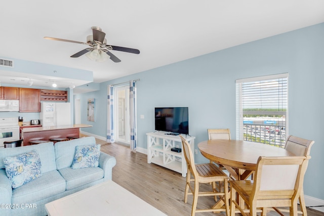 living area featuring visible vents, baseboards, ceiling fan, and light wood finished floors