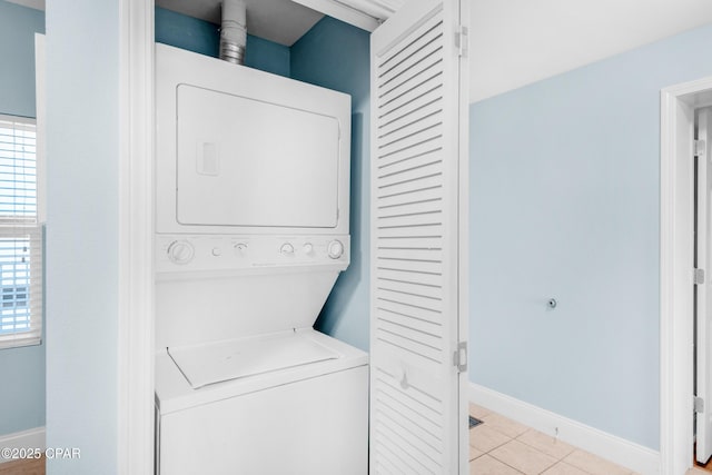 clothes washing area featuring stacked washer / drying machine, baseboards, light tile patterned flooring, and laundry area