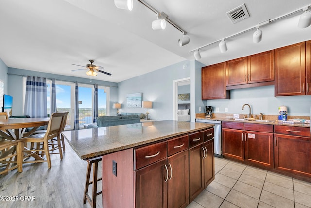 kitchen with a sink, light stone counters, ceiling fan, dishwasher, and visible vents