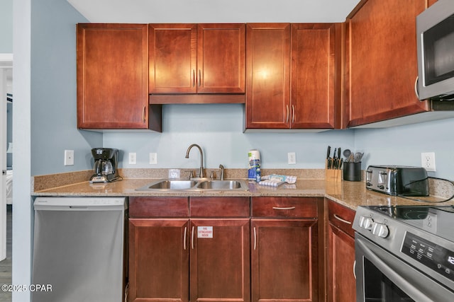 kitchen with a toaster, light stone countertops, appliances with stainless steel finishes, reddish brown cabinets, and a sink