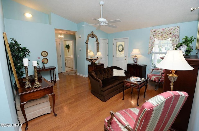 living area with a ceiling fan, a textured ceiling, light wood finished floors, baseboards, and vaulted ceiling