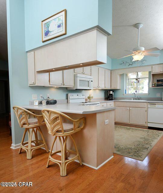 kitchen featuring a sink, white appliances, a high ceiling, a peninsula, and light wood finished floors