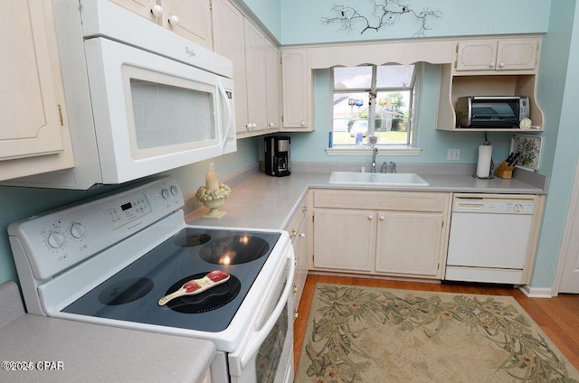 kitchen with light wood finished floors, white appliances, light countertops, and a sink