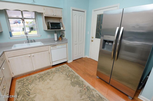 kitchen featuring light wood finished floors, stainless steel fridge with ice dispenser, light countertops, white dishwasher, and a sink