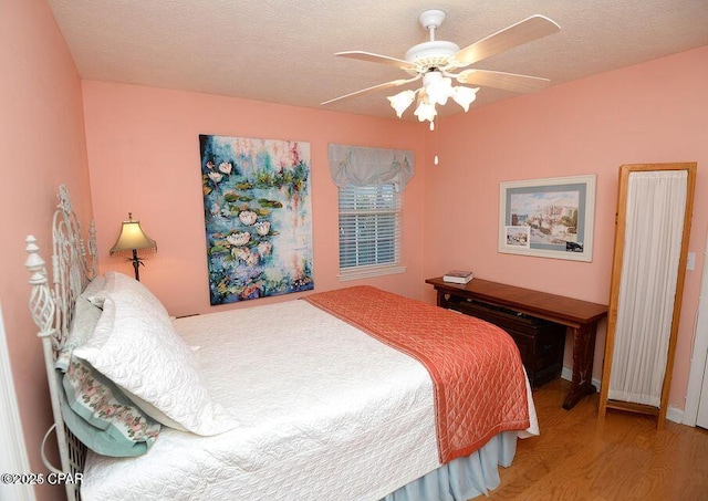 bedroom with a textured ceiling, a ceiling fan, and wood finished floors