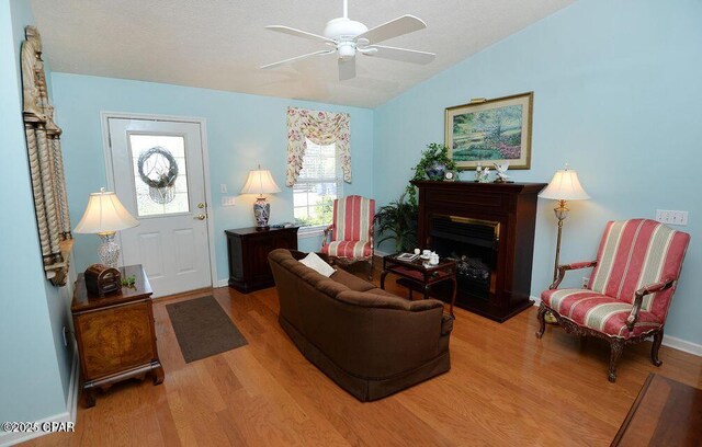 living room featuring a fireplace with raised hearth, light wood-style flooring, a ceiling fan, and lofted ceiling